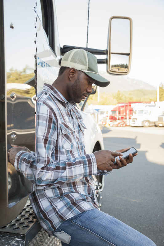 man laying on his truck looking up the insurance number on his phone